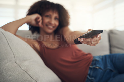 Buy stock photo Defocused shot of a young woman relaxing on the sofa in the living room at home and watching tv