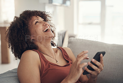 Buy stock photo Shot of an attractive young woman sitting on her sofa in the living room at home and using her cellphone