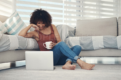 Buy stock photo Shot of an attractive young woman sitting on her living room floor and using her laptop while drinking coffee