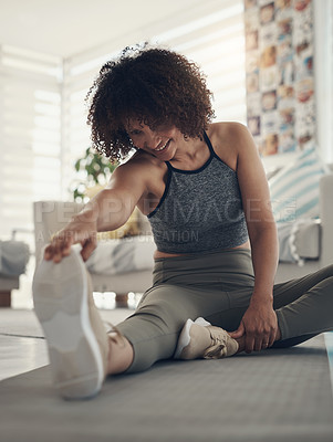 Buy stock photo Shot of an attractive young woman sitting alone in her living room and stretching before working out