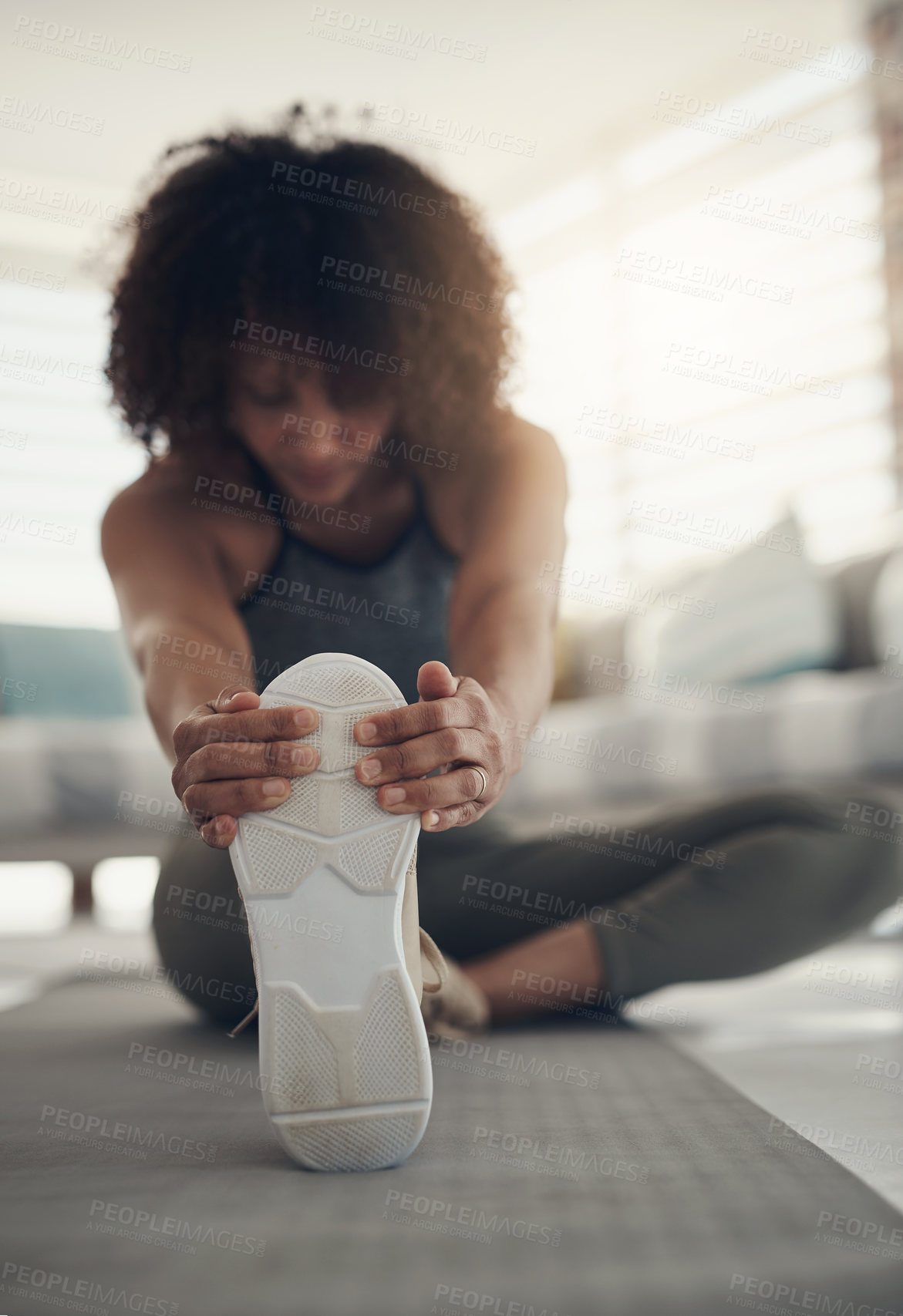 Buy stock photo Defocused shot of a young woman sitting alone in her living room and stretching before working out