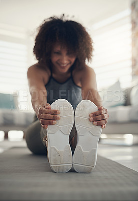 Buy stock photo Defocused shot of a young woman sitting alone in her living room and stretching before working out