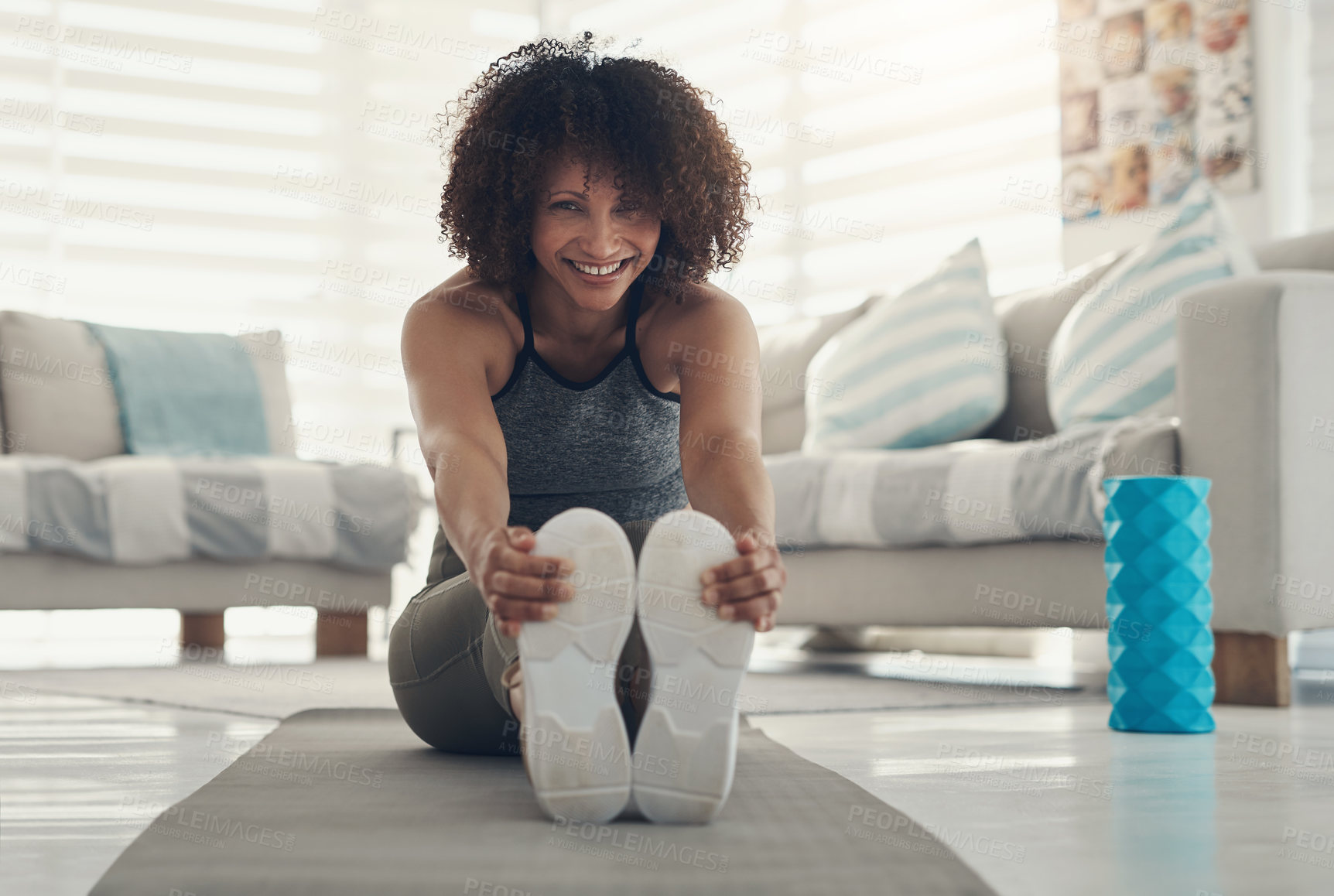 Buy stock photo Shot of an attractive young woman sitting alone in her living room and stretching before working out