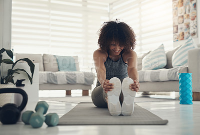 Buy stock photo Shot of an attractive young woman sitting alone in her living room and stretching before working out