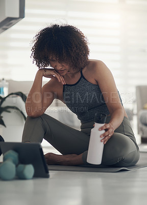 Buy stock photo Shot of an attractive young woman sitting in her living room and watching an online workout routine on a digital tablet