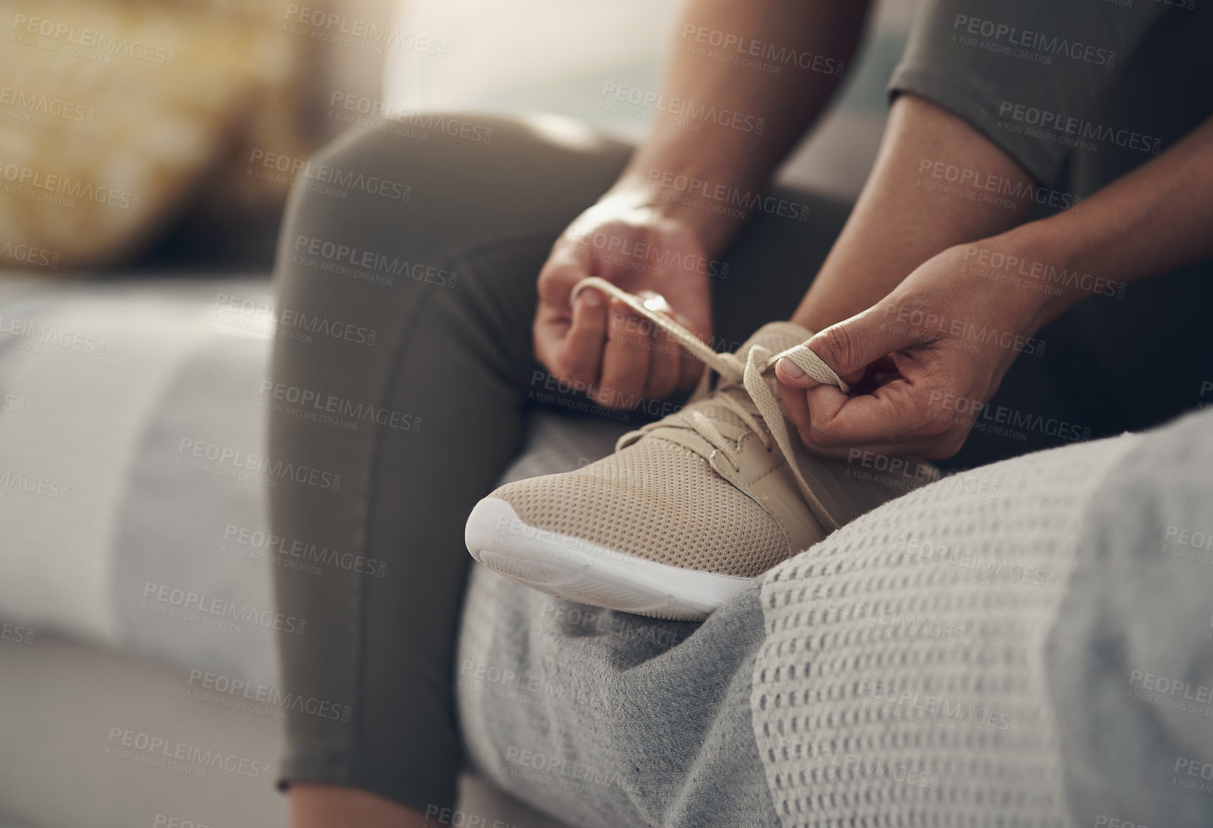 Buy stock photo Cropped shot of an unrecognizable woman sitting alone on her sofa at home and tying her shoelaces before working out