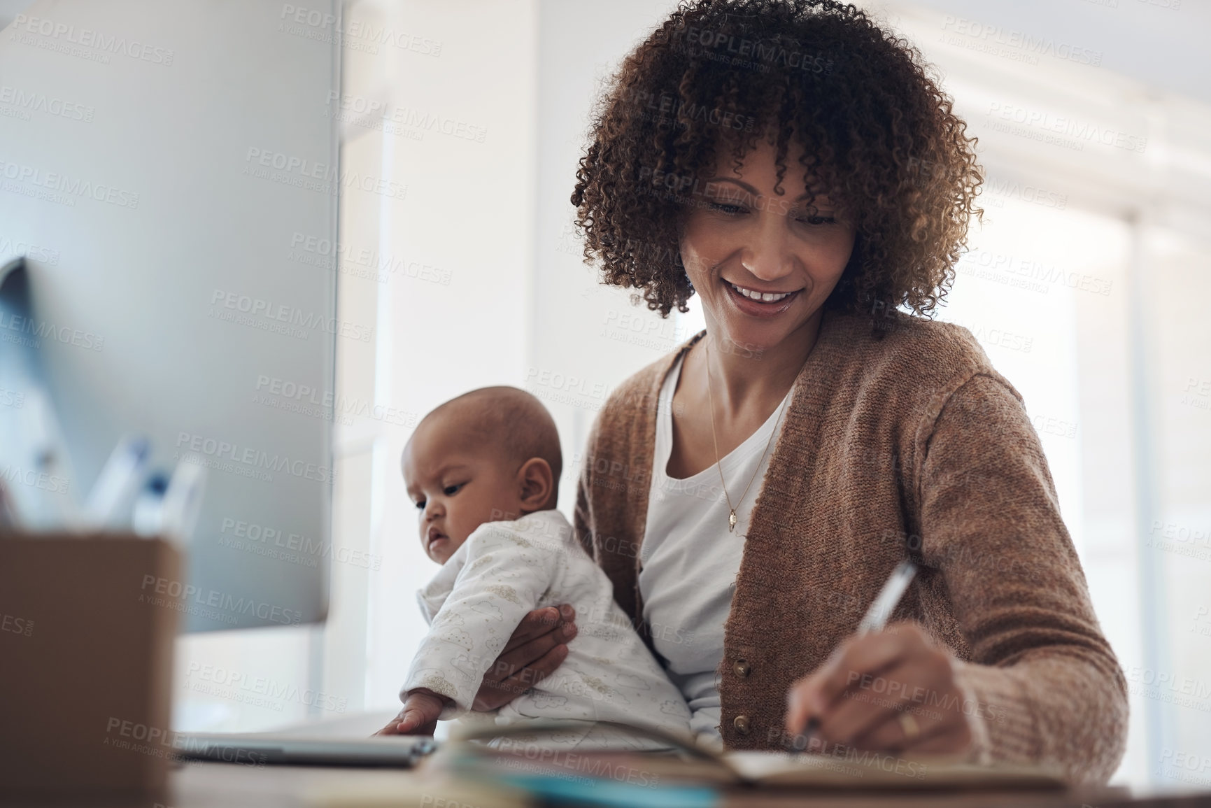 Buy stock photo Shot of a young woman making notes while caring for her adorable baby girl and working at home