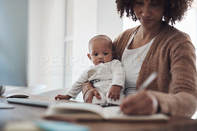 Buy stock photo Shot of a young woman making notes while caring for her adorable baby girl and working at home