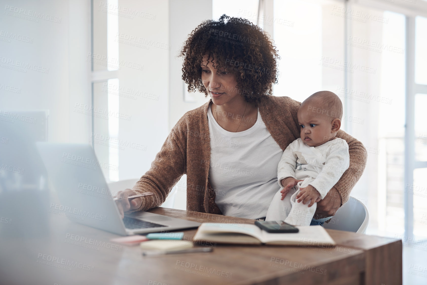 Buy stock photo Shot of a young woman using a laptop while caring for her adorable baby girl at home