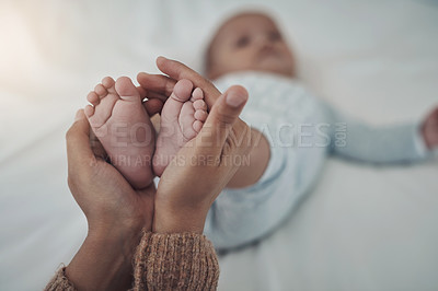 Buy stock photo Shot of an unrecognisable woman holding her baby’s feet on the bed at home