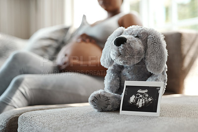 Buy stock photo Closeup shot of a sonogram alongside a stuffed teddybear with a pregnant woman sitting in the background