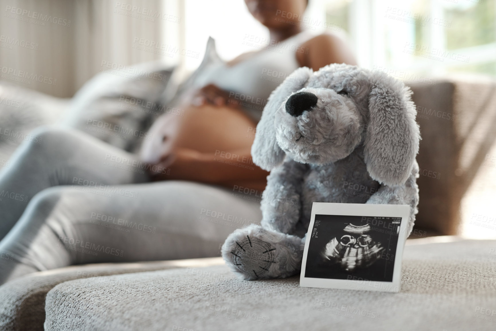 Buy stock photo Closeup shot of a sonogram alongside a stuffed teddybear with a pregnant woman sitting in the background