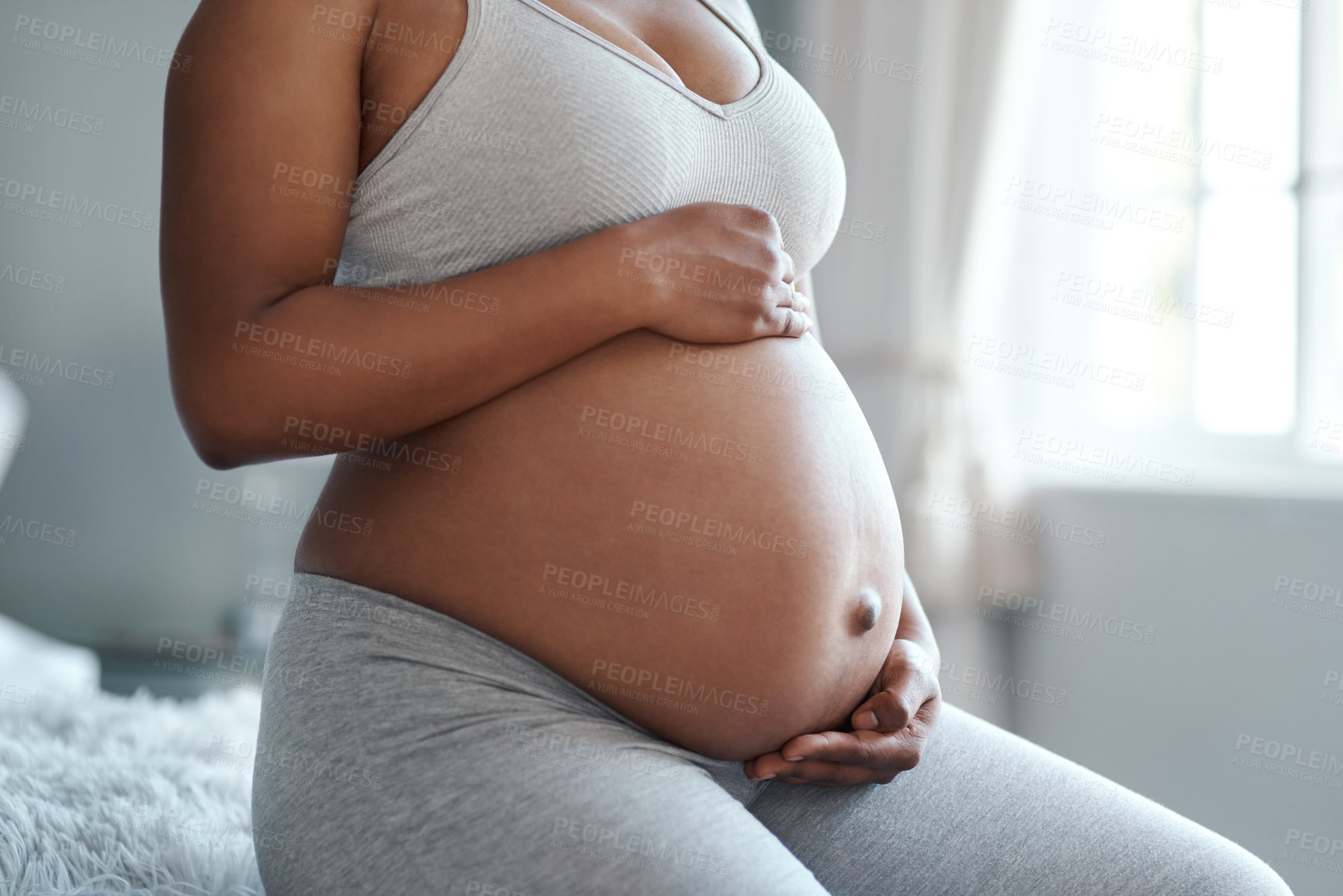 Buy stock photo Closeup shot of an unrecognisable woman touching her pregnant belly at home