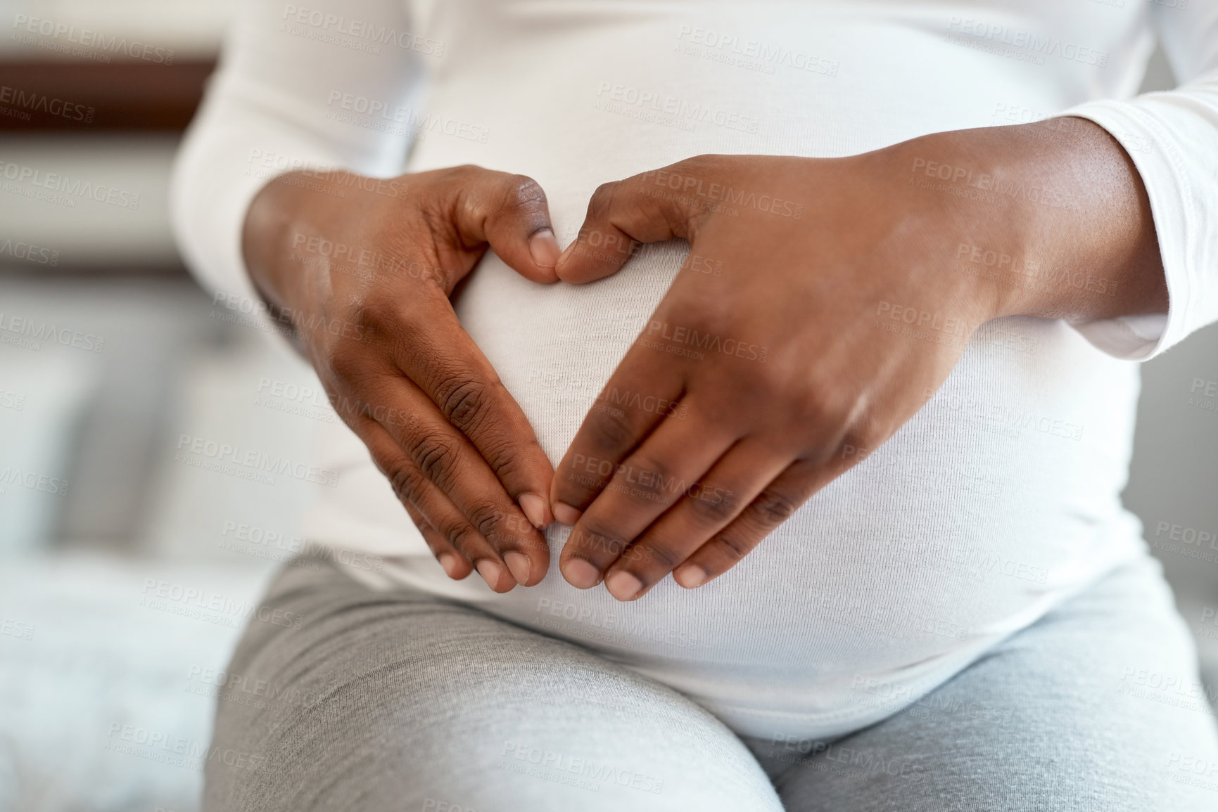 Buy stock photo Closeup shot of an unrecognisable woman making a heart shape with her hands on her pregnant belly at home