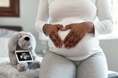 Buy stock photo Closeup shot of an unrecognisable woman making a heart shape with her hands on her pregnant belly at home