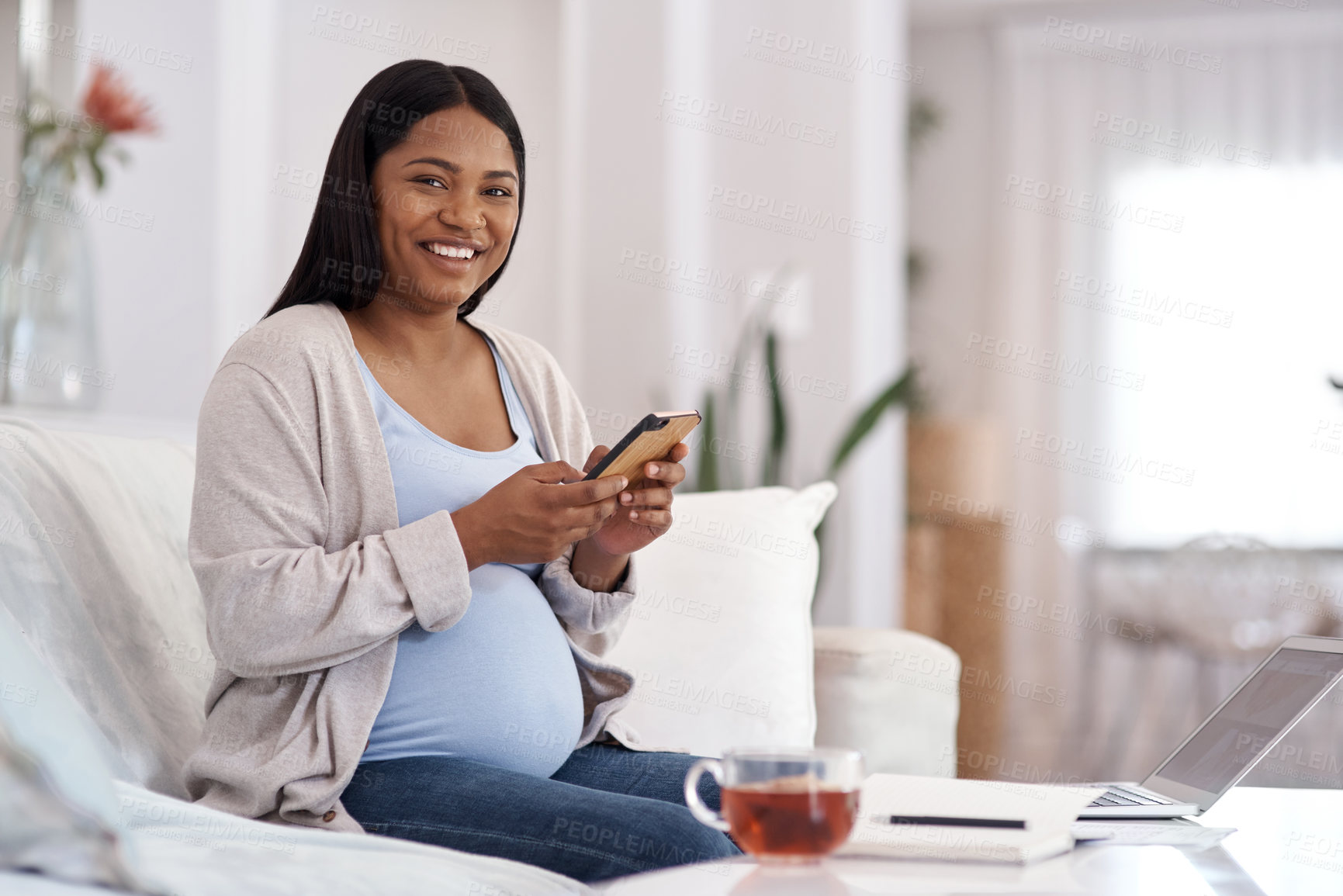 Buy stock photo Shot of a pregnant woman using her cellphone while sitting at home