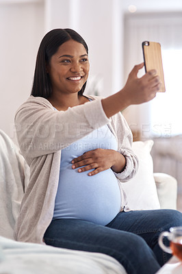Buy stock photo Shot of a pregnant woman taking a selfie while sitting on the sofa at home
