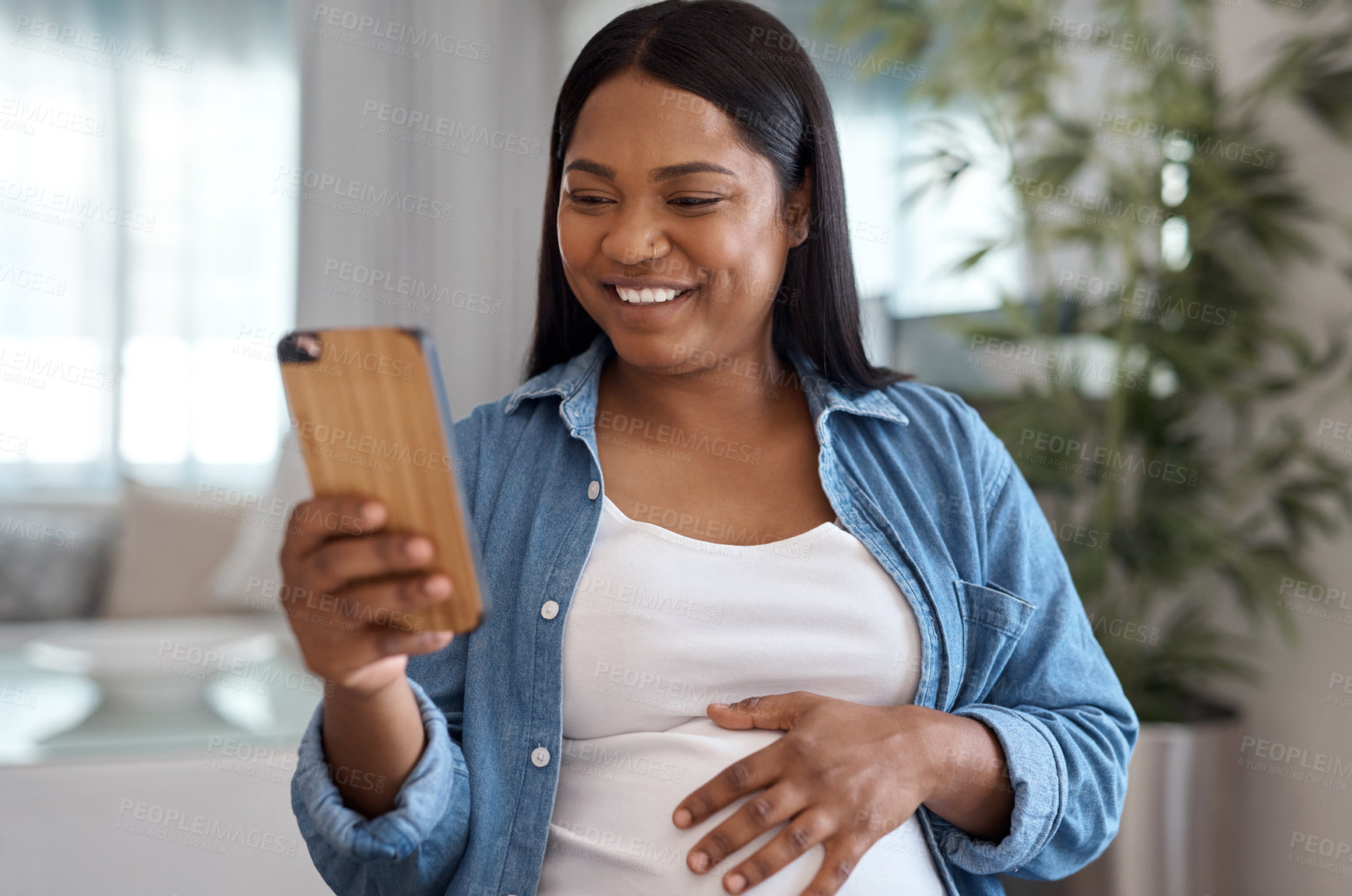 Buy stock photo Shot of a pregnant woman using her cellphone while sitting at home