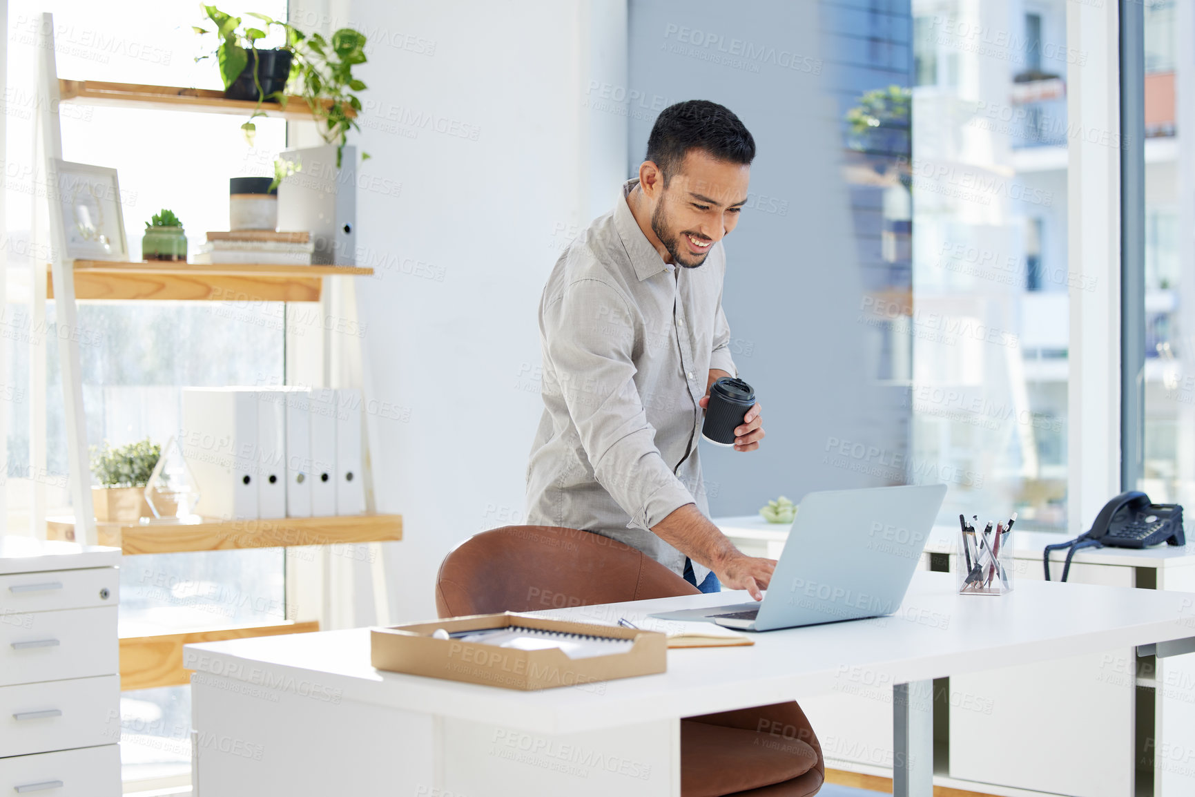 Buy stock photo Shot of a young man using his laptop at work in a modern office