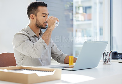 Buy stock photo Shot of a young man using his laptop and having coffee at work in a modern office