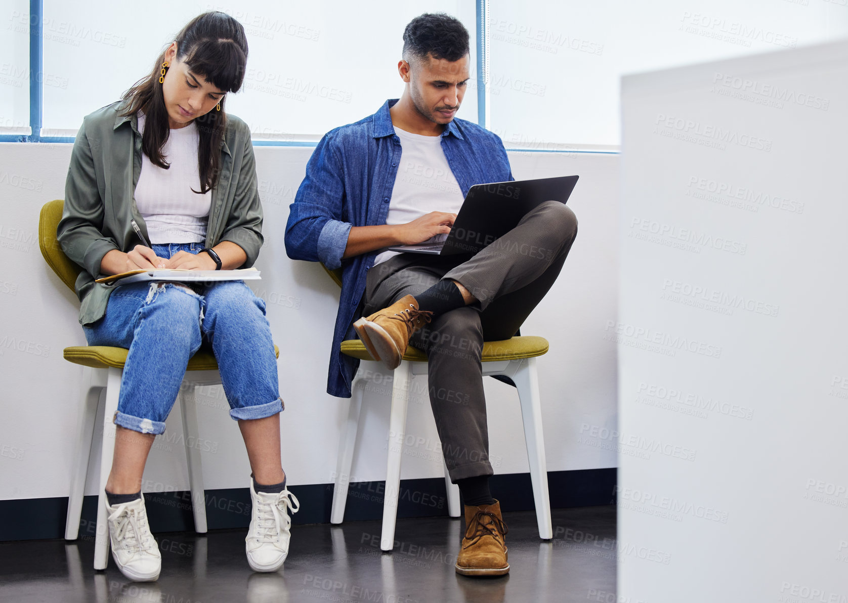 Buy stock photo Shot of two young adults using their devices while waiting to be interviewed in a modern office
