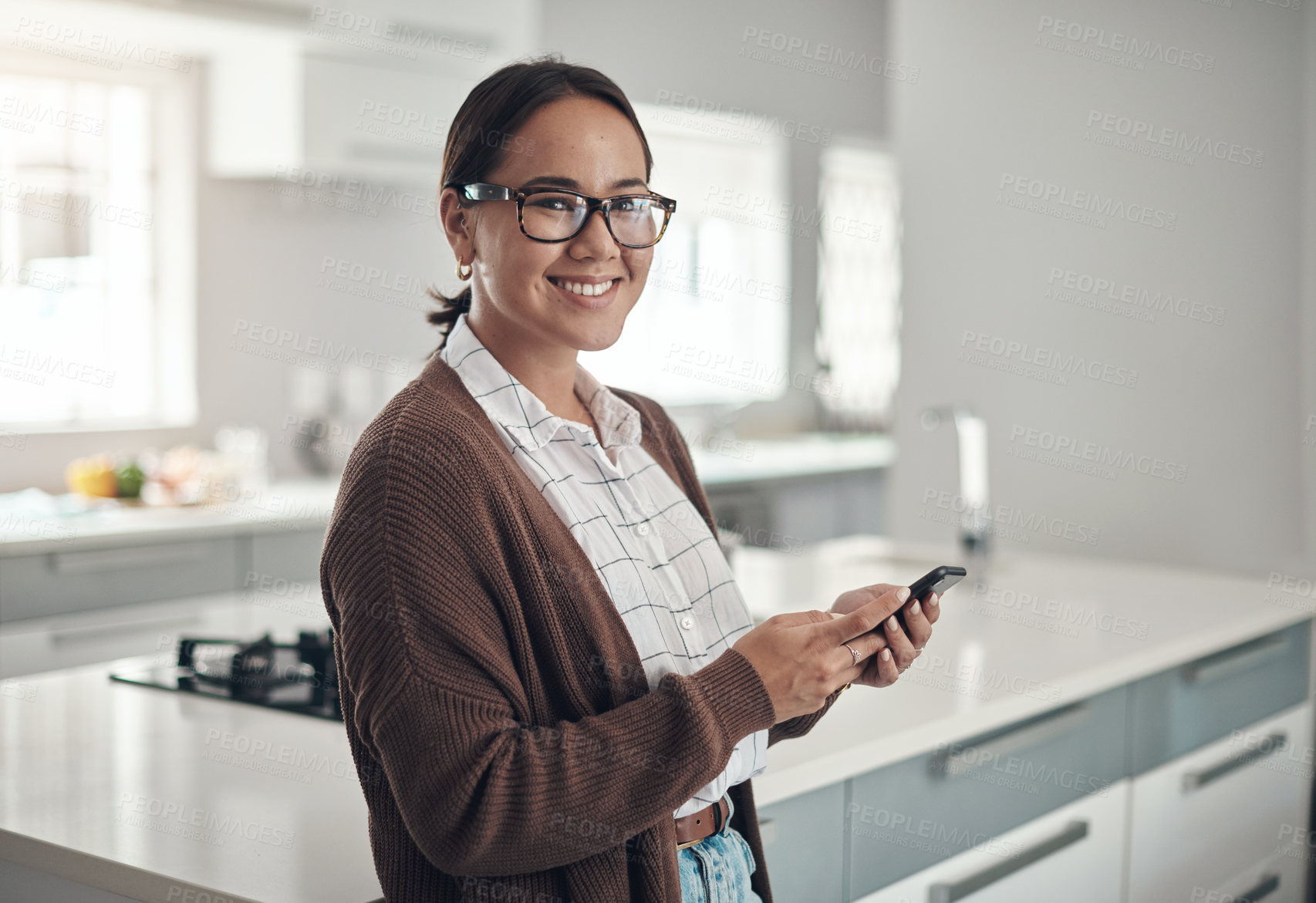 Buy stock photo Portrait of a young woman using a cellphone in the kitchen at home