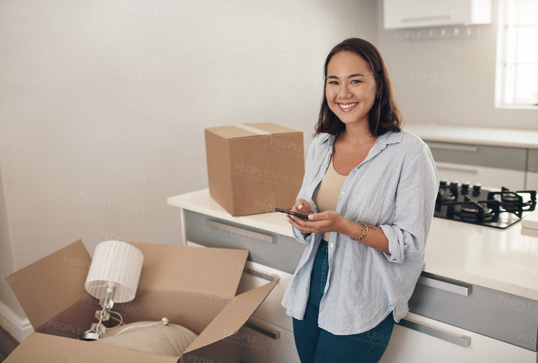 Buy stock photo Portrait, Asian woman and happy in home with boxes for unpacking, satisfied and confident with ownership. Real Estate, smile and furniture in kitchen with smartphone for communication and moving in