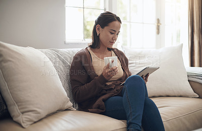 Buy stock photo Shot of a young woman using a digital tablet while drinking coffee at home