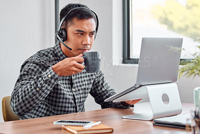 Buy stock photo Cropped shot of a handsome young male call center agent drinking coffee while working on his laptop
