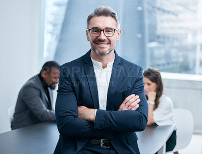 Buy stock photo Portrait of a confident mature businessman standing in an office with his colleagues in the background