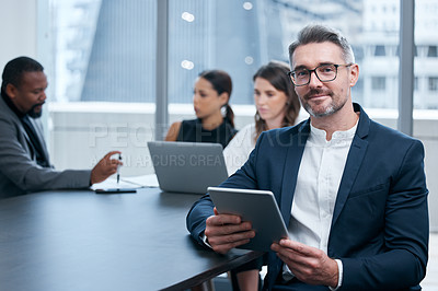 Buy stock photo Portrait of a mature businessman using a digital tablet in an office with his colleagues in the background