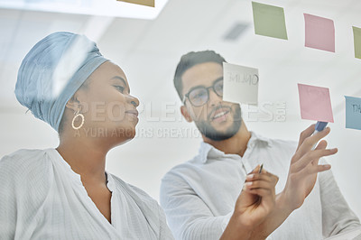 Buy stock photo Cropped shot of two diverse young businesspeople working on a glass wipe board in the boardroom