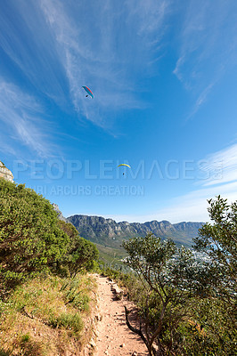 Buy stock photo Nature park landscape with plants and an outdoor dirt path. Beautiful outdoors view of a hiking trail in the mountains during summer. Mountain background with a blue sky and paragliding travelers. 