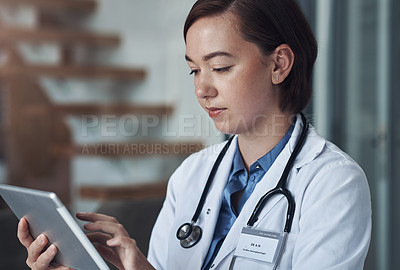 Buy stock photo Shot of a young female doctor taking a break to use her digital tablet