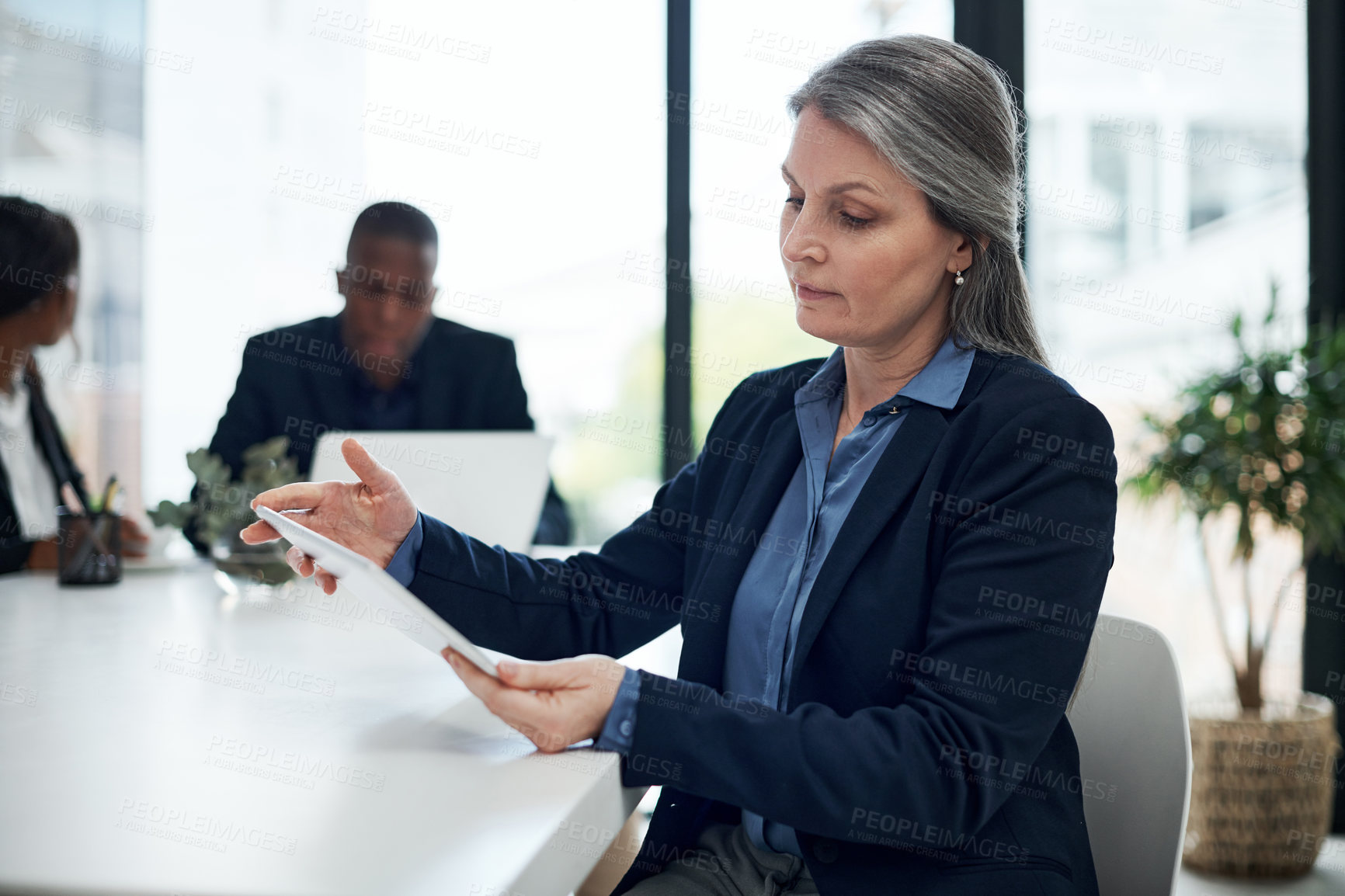Buy stock photo Mature businesswoman, tablet and table in office for meeting, discussion and explanation with team. Female manager, thinking and planning in workplace for research, networking and communication