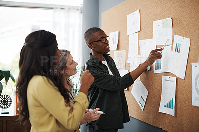 Buy stock photo Side shot of a group of businesspeople brainstorming and sharing ideas on a backboard in a modern office