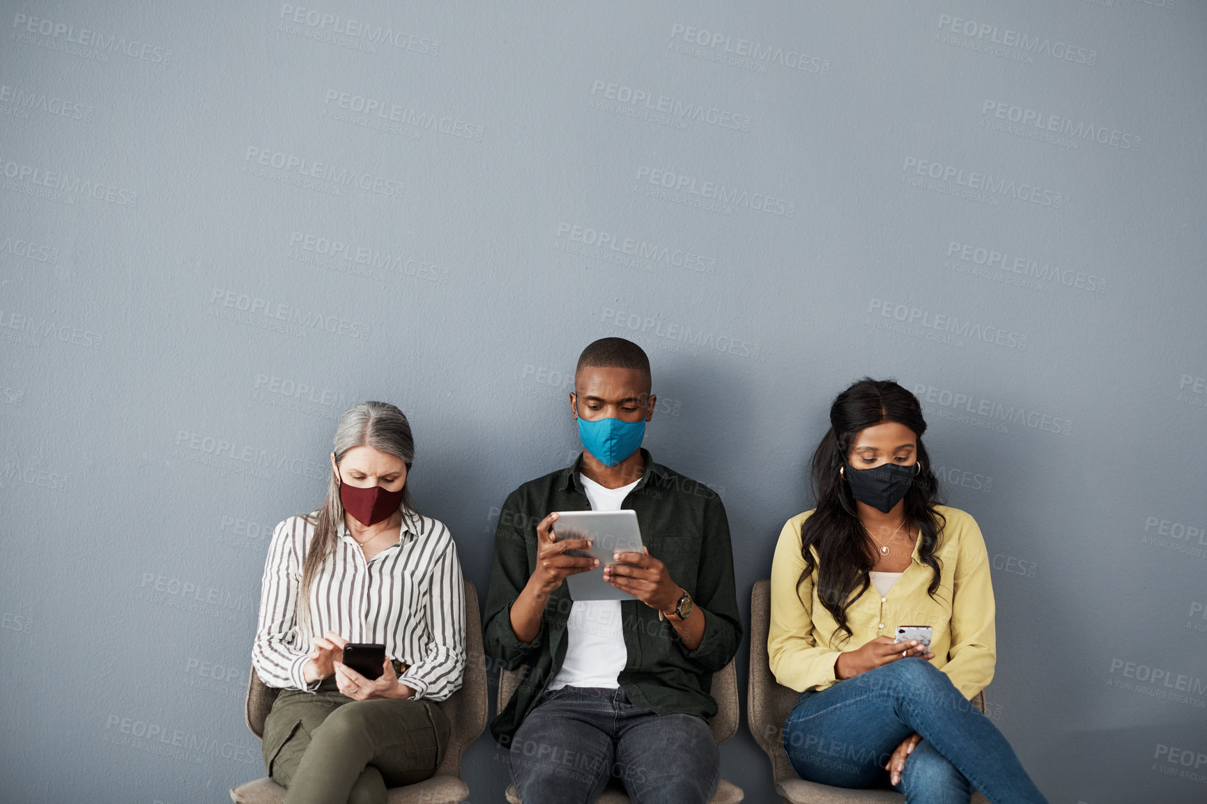 Buy stock photo Shot of a cautious group of people socially distancing while using their smart devices against a grey wall