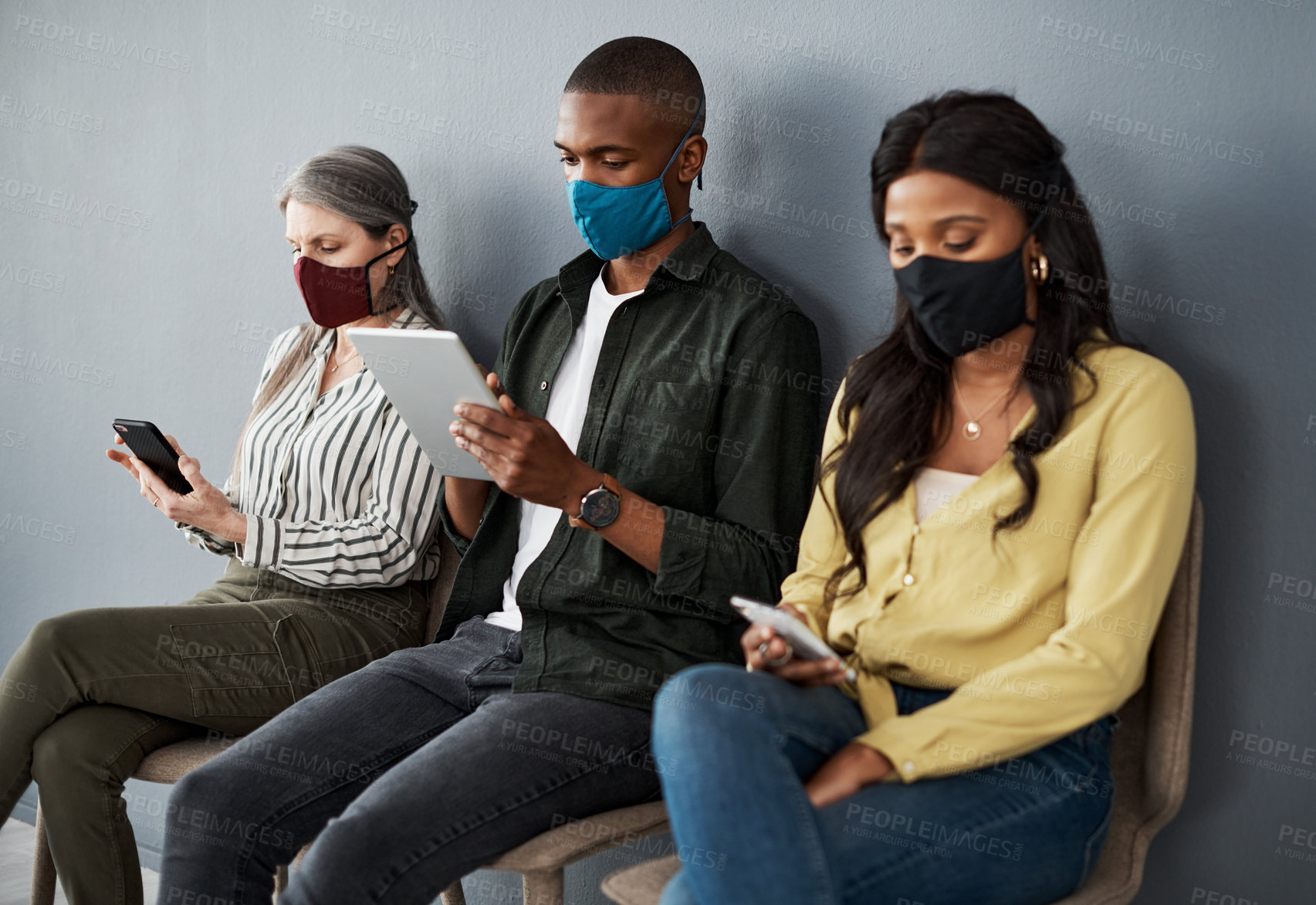 Buy stock photo Shot of a cautious group of people socially distancing while  using their smart devices against a grey wall