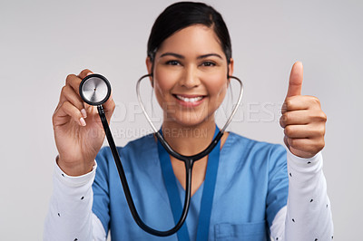 Buy stock photo Portrait of a young doctor showing thumbs up and holding a stethoscope against a white background