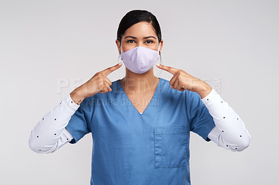 Buy stock photo Portrait of a young doctor pointing to her surgical face mask against a white background