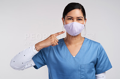 Buy stock photo Portrait of a young doctor pointing to her surgical face mask against a white background