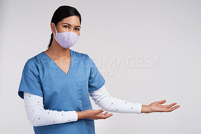 Buy stock photo Shot of a young doctor wearing a surgical face mask and gesturing to her left against a white background