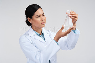 Buy stock photo Cropped shot of an attractive young female scientist examining a beaker filled with liquid in studio against a grey background