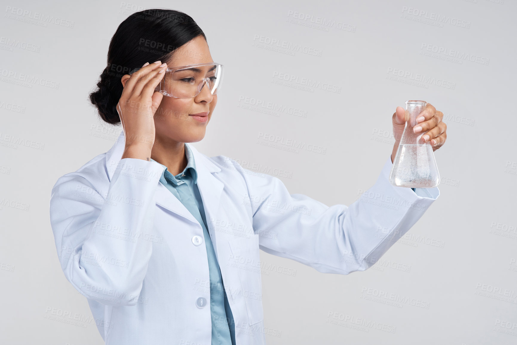 Buy stock photo Cropped shot of an attractive young female scientist examining a beaker filled with liquid in studio against a grey background