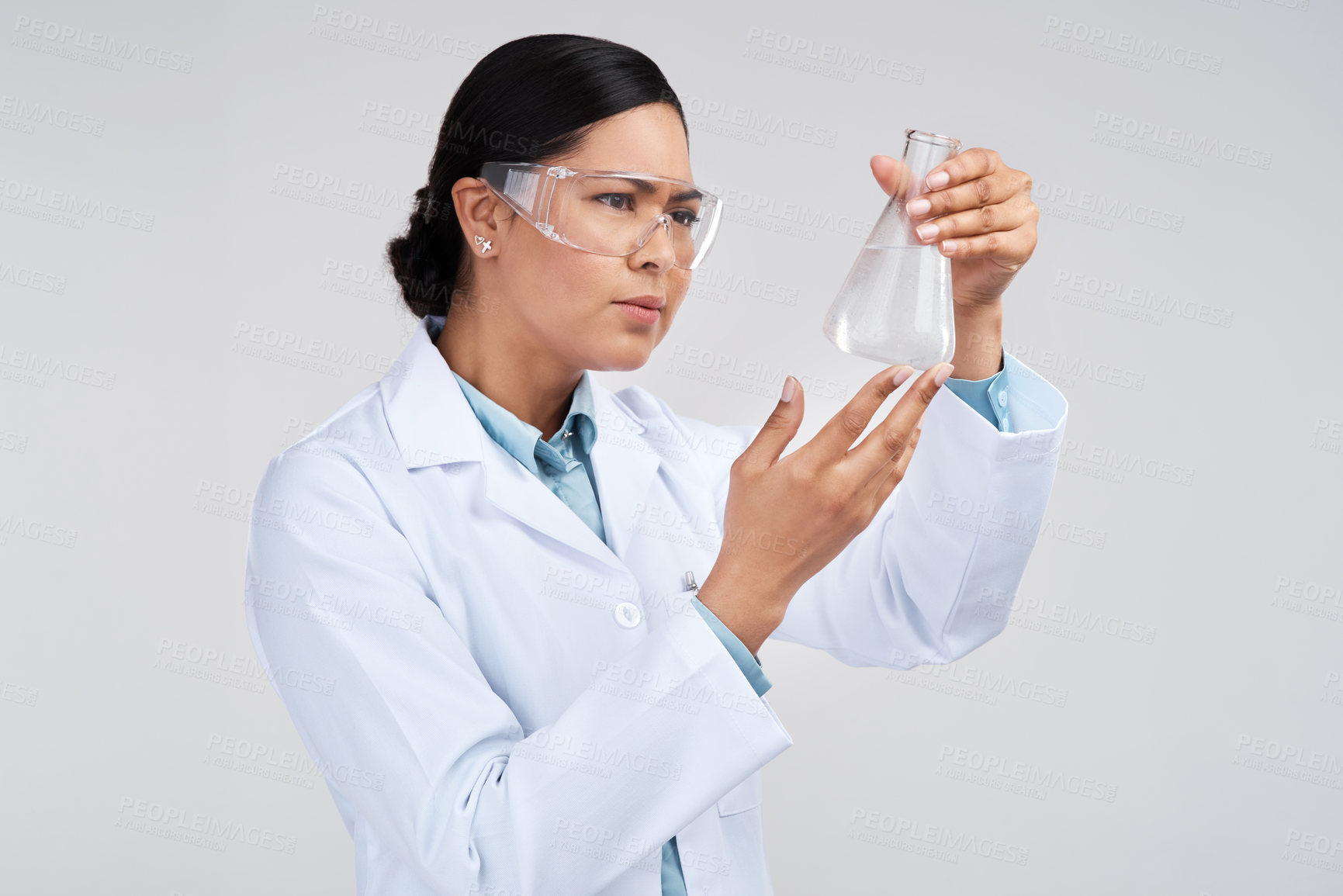 Buy stock photo Cropped shot of an attractive young female scientist examining a beaker filled with liquid in studio against a grey background