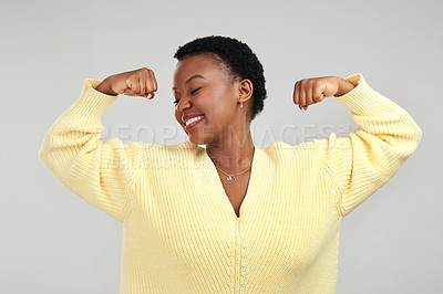 Buy stock photo Shot of a young woman flexing while posing against a grey background