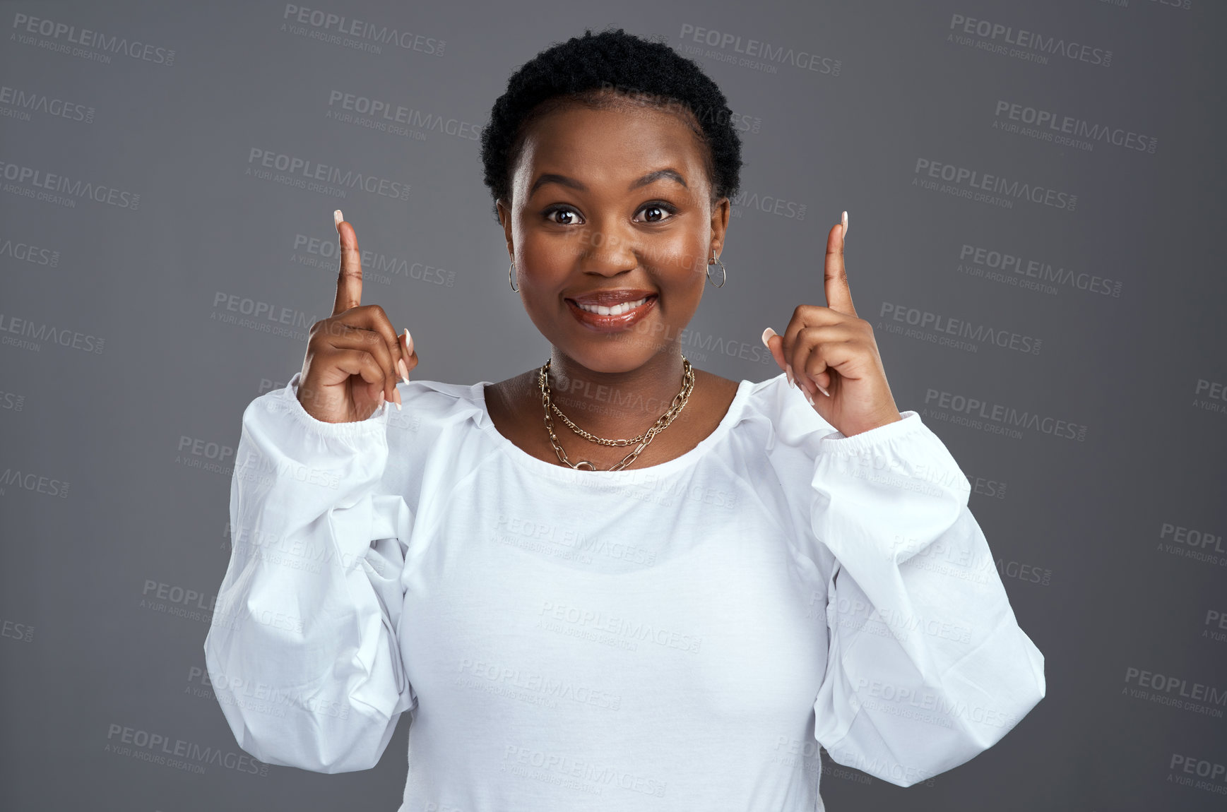 Buy stock photo Shot of a young woman pointing at copy-space while posing against a grey background