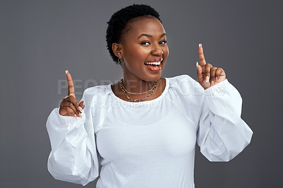 Buy stock photo Shot of a young woman pointing up while posing against a grey background