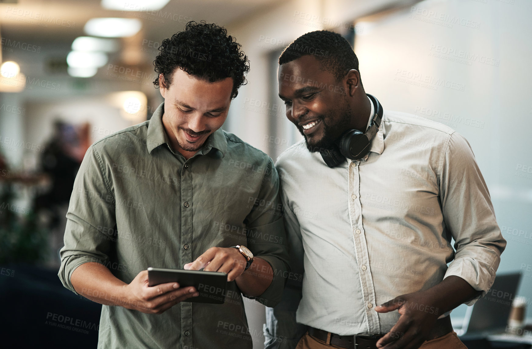 Buy stock photo Shot of two young businessmen standing together in the office and using a digital tablet
