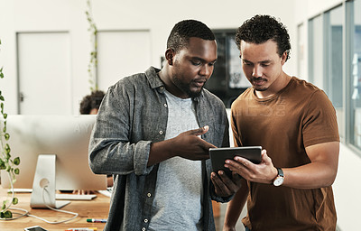 Buy stock photo Shot of two young businessmen standing together and using a digital tablet in the office